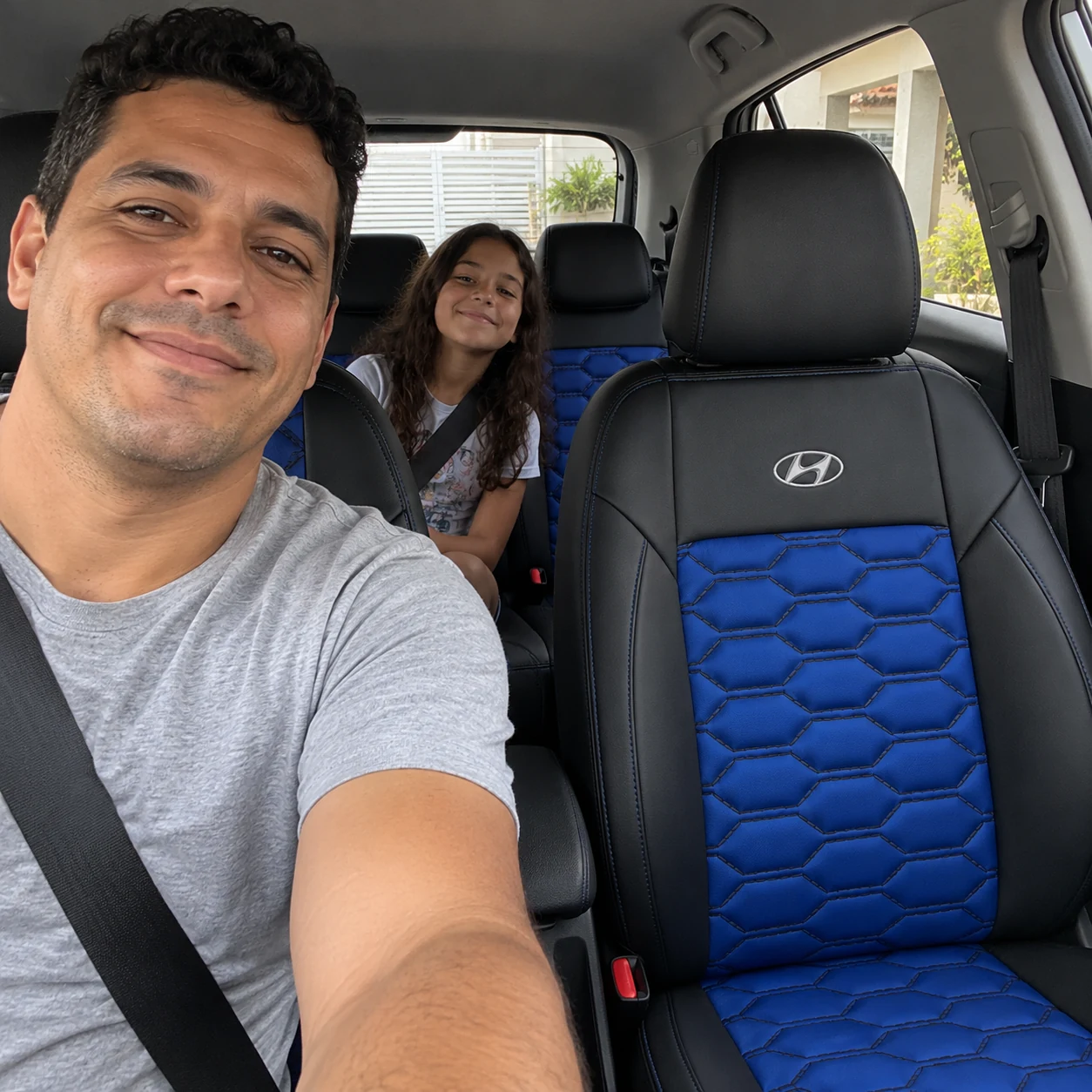 Diego de camiseta cinza com a filha no banco traseiro do Hyundai HB20 com bancos Colmeia pretos com azul royal